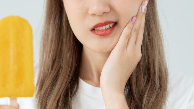 The woman, holding her cheeks, is thinking about what not to eat after a tooth extraction.