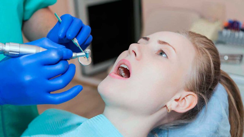 A lady opening her mouth during a root canal treatment from a dentist wearing blue surgical gloves