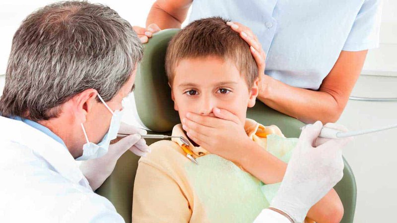 A boy being comforted while covering his mouth while visiting a children’s emergency dentist