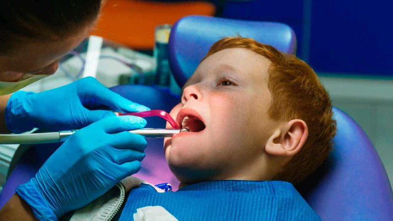 A 24-hour pediatric emergency dentist performs emergency care on red-haired boy during a visit
